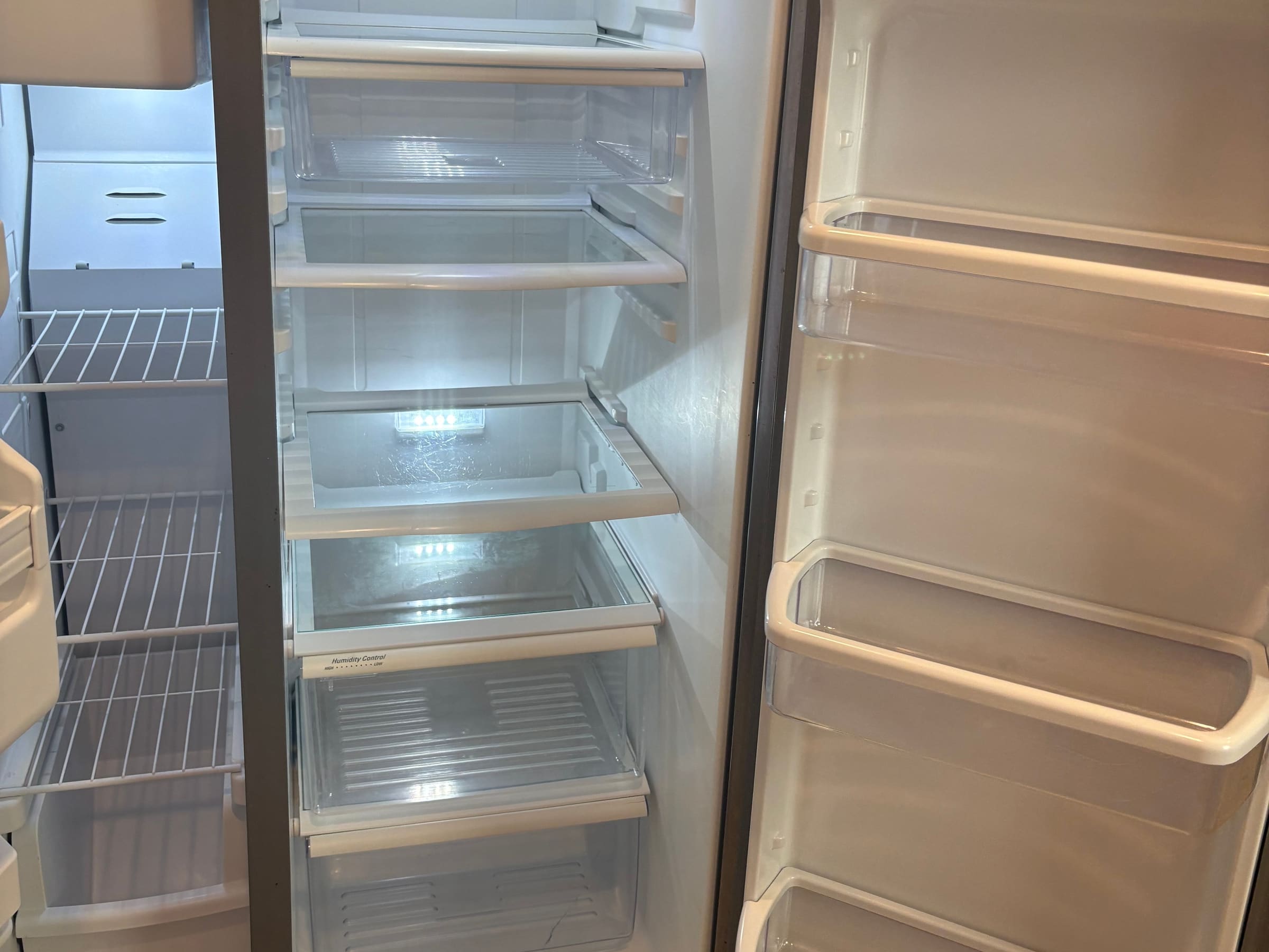 The inside of an emptied refrigerator after a move-out clean, shelves and door bins wiped down.